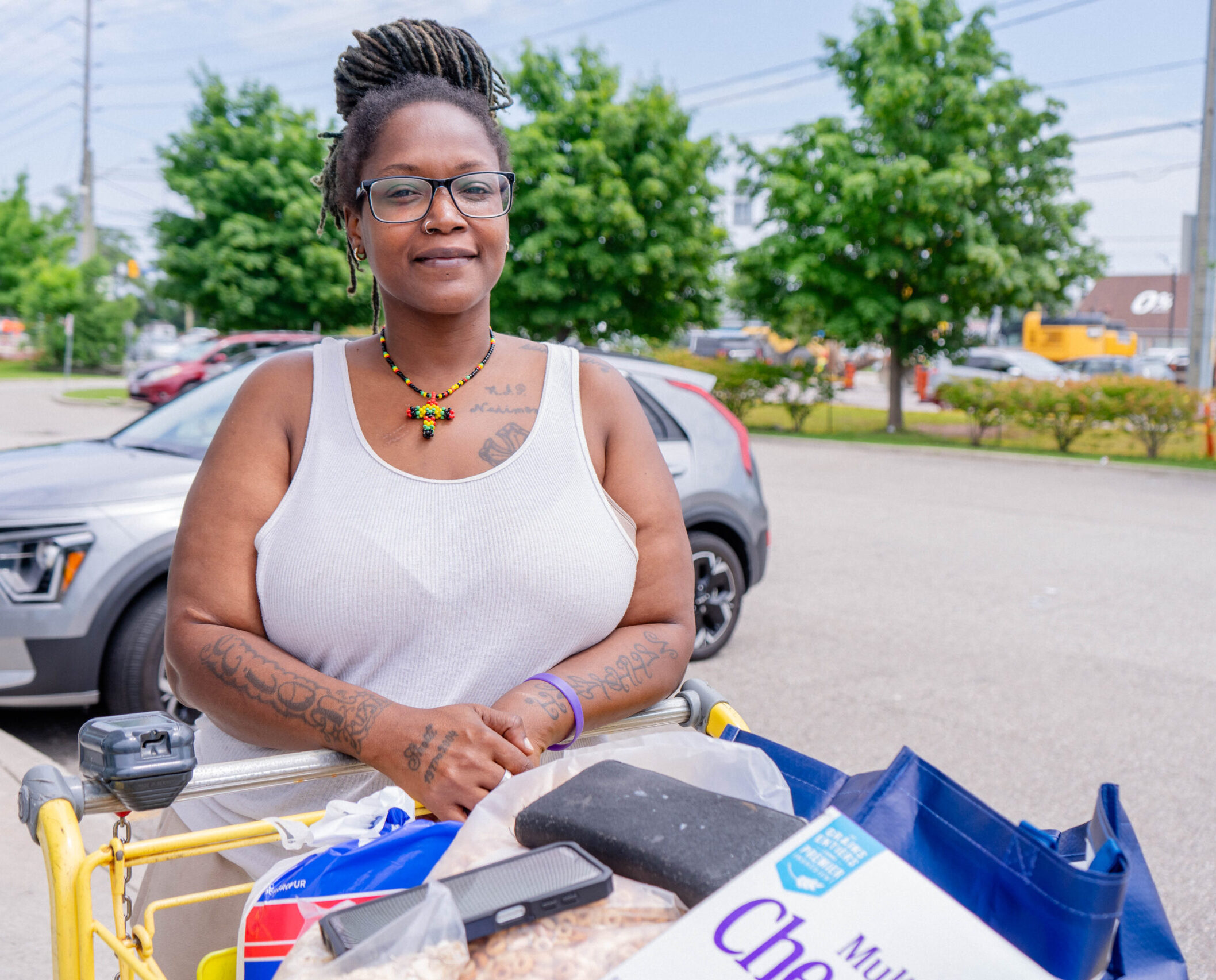 A woman in a tank top standing behind a shopping cart with food products.